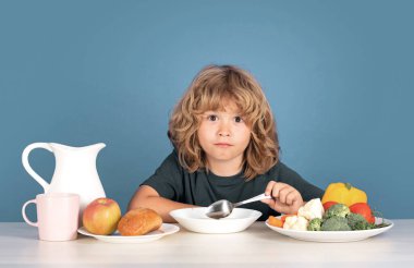 Çorba içen çocuk. Çocuklar için sağlıklı bir kahvaltı. Çocuk yemek yiyor ve çorba içiyor. Çocuğun organik gıda, yoğurt ve süt yiyişinin yakından görüntüsü. Çocuklar sağlıklı beslenir. Gülümseyen küçük çocuk mutfakta yemek yiyor.