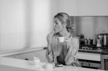 Seksi bir kadın mutfakta kahve içer. Ev mutfağında göğüslerini rahatlatan seksi pijama giyen bir kadın. Baştan çıkarıcı iç çamaşırlı genç seksi ev hanımı mutfakta kahve hazırla.