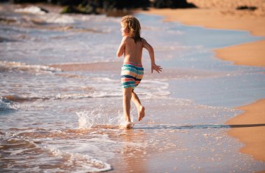 Aktif küçük bir çocuk tatil günlerinde deniz dalgalarında su sıçratıyor. Çocuklarla aile tatili kavramı