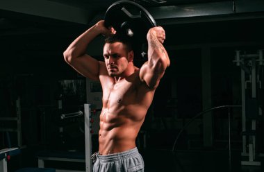 Spor salonunda ağırlık kaldırıcının portresi. Ağır diski olan vücut geliştirici pazılarını çalıştırıyor.