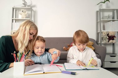 Anne ve iki oğul beraberler, resim yapıyorlar. Annem çocuklara yardım ediyor. Öğretmen okulda okul çocuğuna yardım ediyor. Anaokulunda çizim yapan çocuklar