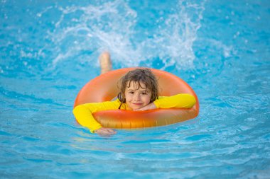 Çocuk yüzme havuzunda yüzüyor. Yüzme, yaz tatili. Çocuk şişme yüzükle havuzda yüzüyor. Yüzme havuzunda şişme yüzüğü olan çocuk. Yaz tatili. Çocuk yüzme. Çocuk deniz suyunda yüzüyor.