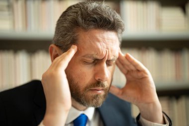 Baş ağrısı olan stresli bir adamın portresi. Yorgun bir adam, elinde gözlük tutarken acı hisseder... tahriş olmuş gözleri ovalar... bilgisayar işinden yorgun düşmüş, stresli bir adam baş ağrısından muzdarip olur.