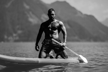 Kürek tahtasıyla güçlü bir kas modeli uydur. Kürek çeken bir adam. Sup board paddle sörfünde güçlü İspanyol adam. İsviçre 'deki Alps Gölü' nde yaz tatilinde SUP sörfü