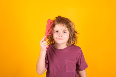 Kıvırcık sarı saçlı, taraklı taraklı komik çocuk. Çocuk saç bakımı. Sarışın, uzun saçlı çocuk saçlarını taramaya çalışıyor. Taraklı bir saç portresi.