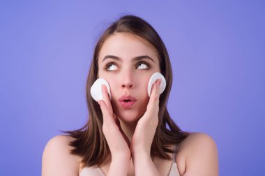 Pamuk yastıklı güzel bir kadın, yüzüne losyon sürüyor, makyajı kaldırıyor. Cilt bakımı. Pamukla yüzünü temizleyen bir kızın stüdyo portresi, izole bir arka plan. Yüz toneri ve pamuk pedi