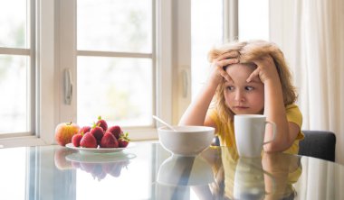 Unhappy little boy child sit at table at home kitchen have no appetite for healthy breakfast. Upset kid refuse to eat cereals with milk. Adorable sad tired kid eating low fat soy milk in bowl cereal