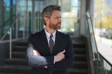 Businessman standing outdoor on modern office building. Business success. Business man thinking outdoor. Modern businessman in full suit standing outdoors near office cityscape
