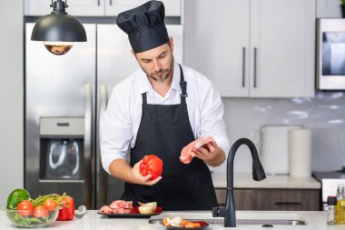Aşçı mutfakta sebzelerle yemek pişiriyor. Sağlıklı yemek. Mutfakta yemek pişiren çekici beyaz adam. Modern mutfakta sağlıklı yemek pişiren adam. Şef mutfakta yemek hazırlıyor.