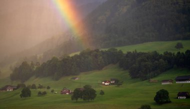 Alp köyü yağmuru. İsviçre. İsviçre 'de alp gökkuşağı manzarası. Lucerne 'deki yeşil Alpler' in panoramik görüntüsü. Yaz dağlarında inanılmaz bir manzara. Güneş ışığı ve gökkuşağındaki çayırlar