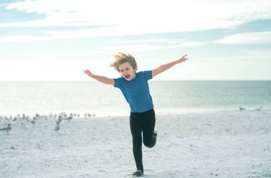Mutlu çocuk koşuyor, kuşları kovalıyor. Mutlu çocuk martı kuşlarıyla koşuyor, sıcak bir yaz gününde kumsalda eğleniyor. Yaz tatili