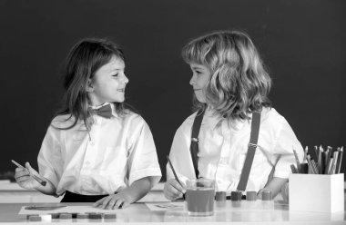 Sınıfta karatahta arka planda komik öğrenciler çiziyor. Okul arkadaşları çocuklar, kız ve erkek birlikte resim yapıyorlar. En iyi çocuklar arkadaşlığın tadını çıkarır