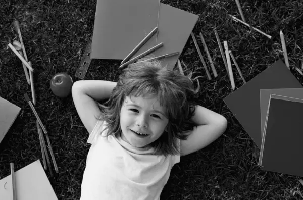 stock image Portrait of a happy pupil school boy lying on the grass. School dream. Daydreamer school child. Dreams and imagination. Dreamy school kid face