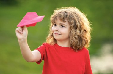 Çocuk kağıt uçakla oynuyor. Yaz günü parka kağıt uçak atan sevimli bir çocuk. Mutlu çocuk gökyüzüne karşı kağıt uçakla oynuyor. Kağıttan uçağı olan bir çocuk. Oyuncak uçak