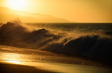 Denizde altın gün batımı. Okyanusun üzerinde günbatımı olan manzara. Altın gökyüzü ve okyanus suyu. Dalgalar sıçrıyor