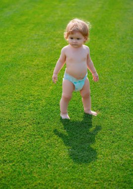 Yeşil çimlerde poz veren sevimli erkek bebek. Çimlerde güzel bir çocuğun yaz portresi