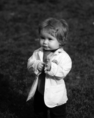 Bahçede eğlenen beyaz bir çocuğun portresi. Bahçede yürürken çimlerin üzerinde bir çocuk. Mutlu çocukluk ve bebek sağlığı hizmetleri. Takım elbiseli, ceketli ve kravatlı komik küçük adam.