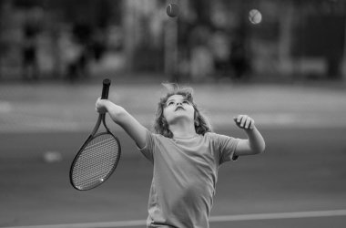 Sahada tenis oynayan bir çocuk. Çocuk tenis raketiyle tenis topuna vurdu. Çocuklar için aktif egzersiz. Çocuklar için yaz etkinlikleri. Çocuk tenis oynamayı öğreniyor. Sport Kid sahada topa vuruyor.