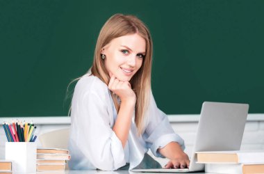 Üniversite sınıfında dizüstü bilgisayarı olan güzel bir genç kızın portresi. Sarışın, güzel kız öğrenci çalışıyor. Tahtada üniversite öğrencisi. Masadaki güzel kız öğrenci. Öğrenci Günü