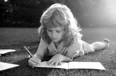 Defterine kalem yazan çocuk. Çocuk okulu ve açık hava eğitimi. Doğa ve park. Erken öğrenme. Açık havada yaz