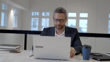 Orta yaşlı iş adamı ofiste dizüstü bilgisayarla çalışıyor. İspanyol iş adamı dizüstü bilgisayar kullanıyor. Milenyum adamı iş yerinde dizüstü bilgisayar kullanıyor. Genel müdür, ofis çalışanı, ofiste çalışan iş adamları.