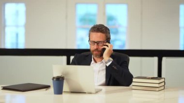 Ofis çalışanı telefonda dizüstü bilgisayarla konuşuyor. İş adamının ofiste telefon görüşmesi var. Modern ofiste iş adamı telefonda konuşuyor. Telefon kullanan bir iş adamı. İş konuşması