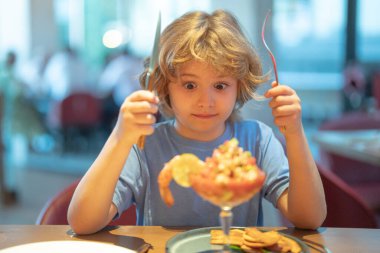 Funny surprised Little boy eating seafood in cafe. Kid eat Food fish gourmet seafood shrimp in restaurant. Adorable little boy at restaurant having breakfast