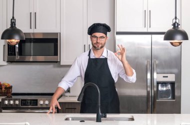 Chef cook with ok sign, delicious food. Portrait of chef man in a chef cap in the kitchen. Man wearing apron and chefs uniform and chefs hat. Character kitchener, chef for advertising