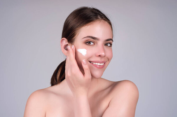 Молодая женщина наносит крем для тела на фоне студии. Обычная красота. Студийное лицо красивой женщины с идеальной кожей. Крем для морщин. Концепция красоты. Женщина наносит крем для лица