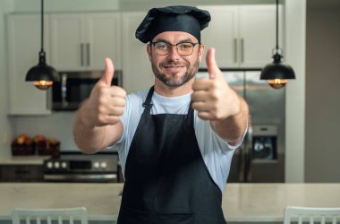 Mutlu aşçı baş parmağı yukarıda. Mutfakta şef üniforması giyen yakışıklı orta yaşlı bir adam. Aşçılık ve aşçılık. Restoran menüsü kavramı