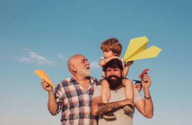 Mutlu çocuk oyuncak kağıt uçakla oynuyor yaz gökyüzü arka planında. Heyecanlı bir öğretmen. Mutlu üç nesil erkekler mavi gökyüzü arka planında eğleniyor ve gülümsüyor. Çoklu nesil