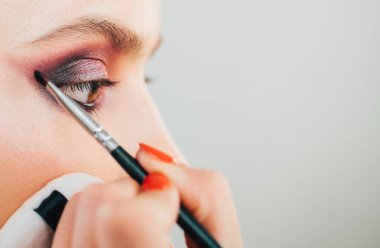 Stüdyodaki profesyonel makyözden lüks makyaj malzemeleri. Vogue, kozmetik ve cazibe konsepti. Kadınların gözlerini parlak mor dumanlı göz makyajıyla kapat.