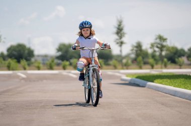 Çocuk yaz parkında bisiklete biniyor. Bisiklet süren kasklı çocuk. Dışarıda bisiklete binen çocuk. Bisiklet süren kasklı çocuk. Küçük çocuk bisiklet sürmeyi öğreniyor. Bisikletli çocuk