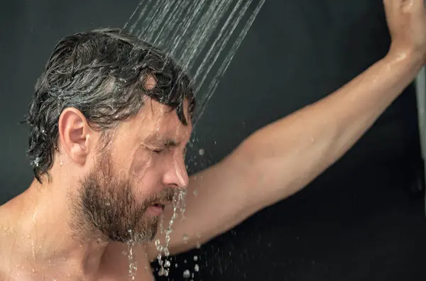 stock image Man washing hair in bathroom. Guy bathing shower head in bathtub. Male face in shower. Man taking shower in bathroom. Guy showering. Bathroom concept. Man is under water drops in bathroom