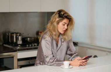 Sinirli ev hanımı mutfakta kahve içer. Sabahları mutfakta telefonda konuşan üzgün bir kadın.