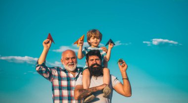 Baba ve büyükbabasıyla birlikte mavi gökyüzü arka planında parkta eğlenen genç bir çocuk. Babalar Günü - Büyükbaba, baba ve oğul kucaklaşıyor ve birlikte eğleniyorlar.