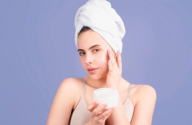 Yüzünde kozmetik krem, cildinde de yumuşaklık var. Vücut bakımı. Havluyla cildine krem süren bir kadın. Spa salonu konsepti. Spa kızı. Mükemmel ciltli güzel bir genç kadın.