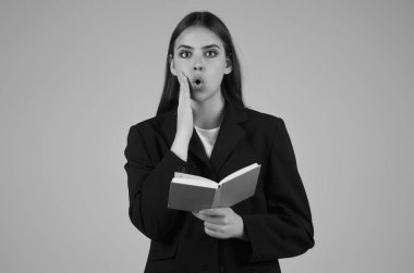 Elinde not defteri olan takım elbiseli genç bir kadın, gri arka planda izole edilmiş. Not defteri olan bir öğrenci. Not defteri düzenleyicisi olan sürpriz öğrenci. Genç iş kadını not defterine yazıyor.