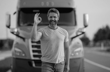 Kamyonun yanında erkek sürücü var. Kamyonetin yanındaki tişörtlü adam. Yakışıklı, orta yaşlı kamyoncu kamyoncu adam. Ulaşım endüstrisi araçları. Kamyonun önündeki yakışıklı adam.