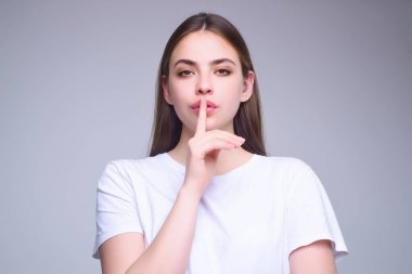 Dudaklarında parmak olan bir kadın. Sessizlik hareketi. Şşş. Stüdyo arka planında izole edilmiş dudaklarda işaret parmağı tutan güzel bir kızın portresi. Şşş işareti gösteren kadın.