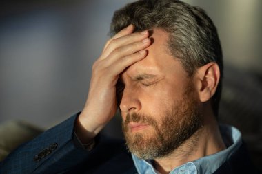 Yorgun adamın korkunç bir baş ağrısı var. Bitkin, sağlıksız hisseden, baş ağrısı hastalığına üzülen bir adam. Stresli orta yaşlı bir adamın baş ağrısı olan portresi. Migren ve baş ağrısı konsepti