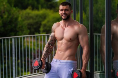 Muscular man workout in the gym. Athletic man having weight training in gym. Handsome man with strong muscles workout in the gym. Portrait of sexy muscular male with dumbbells. Bodybuilder exercise