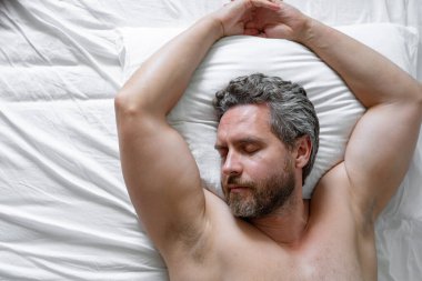 Beyaz yatakta uyuyan adam. Yatak odasında uyuyan seksi üstsüz adam. Latin kökenli olgun bir adam sabahları evde uyuyor. İyi uykular. Yatakta uyuyan adam. İnsanlar yatma vakti, dinlenme zamanı.