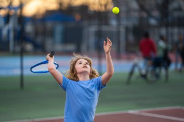 Sahada tenis oynayan bir çocuk. Çocuk tenis raketiyle tenis topuna vurdu. Çocuklar için aktif egzersiz. Çocuklar için yaz etkinlikleri. Çocuk tenis oynamayı öğreniyor. Çocuk sahada topa vuruyor