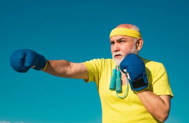 Boks pozisyonunda kıdemli sporcu boks eldivenleriyle egzersiz yapıyor. Yaşlı adam kum torbasına vuruyor. Üst düzey dövüşçüler poz veriyor. Boksu seviyorum.