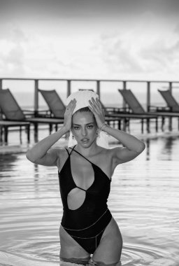 Spa rahatlaması. Havuz suyunun yanında havluyla poz veren zarif seksi kadın.