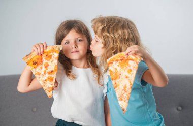 Pizza yiyen aç çocuklar. Mutlu çocuklar pizza yiyor ve birlikte eğleniyorlar. Mutlu çocuklar ellerinde pizza dilimleri ve öpücükler