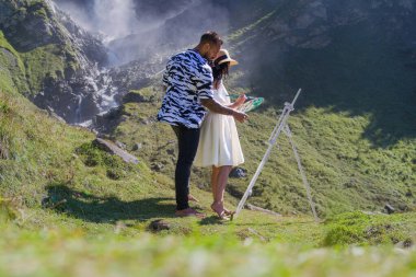 Sanat çifti birlikte doğada yaşıyor. Dağlarda resim yapan aşık sanatçı çift. Şehvetli bir çiftin açık havada çekilmiş bir fotoğrafı kırsal bölgedeki çayırlarda bir resim çiziyor. Doğada romantik bir çift