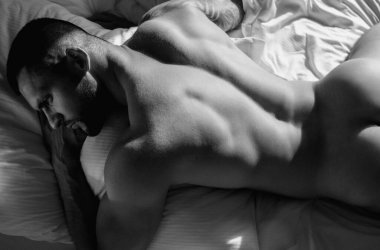 Handsome muscular man lying shirtless in bed. Young handsome man resting on the bed at home. Guy with thletic flexing muscles. Sexy young handsome naked man on bed. Seductive gay