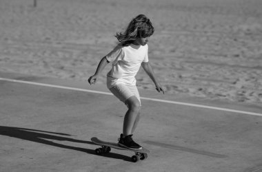 Çocuk kaykaycı parktaki kaykayda biniyor. Genç gülümseyen çocuk modern kruvazör kaykayına biniyor.